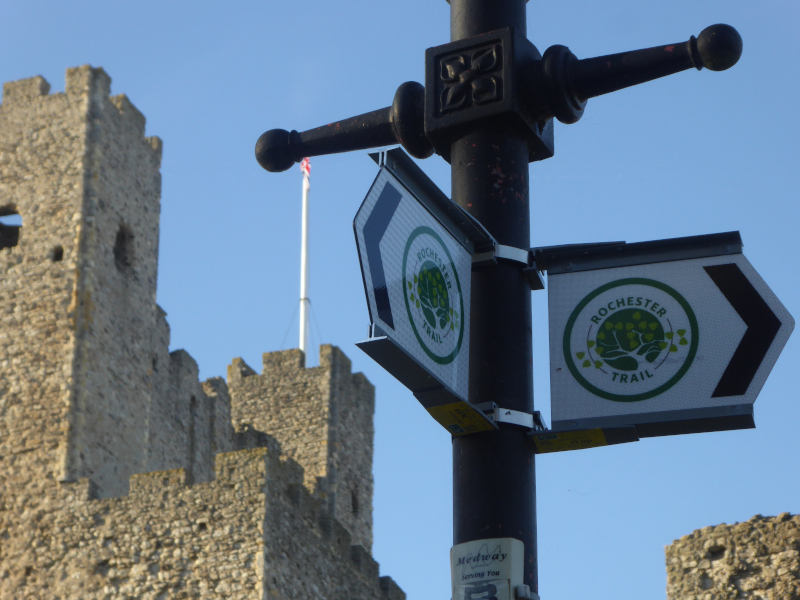 Direction pointers on a traditional black lampost with two symbols indicating the Rochester Trail. A Norman castle is visible in the background.